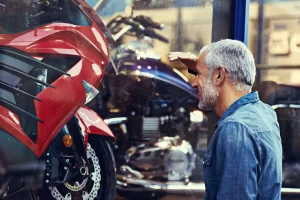 A man is window shopping a new red motorcycle out the front of a showroom considering if he could get a loan for it.