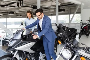 A man in a motorcycle showroom is checking out a new bike he would like to buy with finance while the sales lady looks on in the background