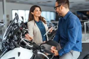 A happy man is chatting with the bike sales woman in the new motorcycle showroom as he sits on the bike he's wanting to buy with finance in 2025